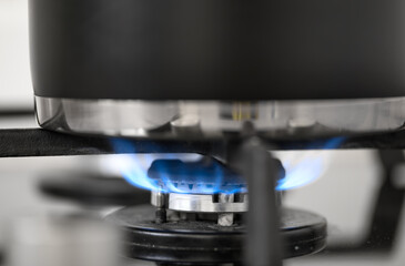 Gas stove burner close-up with blue flame, pot on it