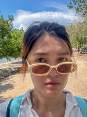 Unhappy asian Thai woman take selfie with bored face, feeling hot while traveling beach in Thailand on sunny day.