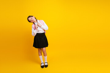 Schoolgirl Posing Playfully with Backpack on Vibrant Yellow Background in Uniform