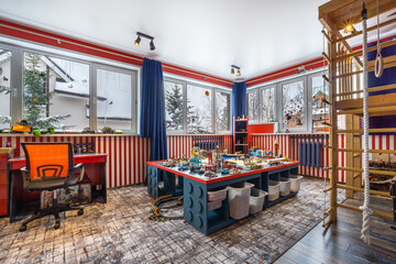 This vibrant playroom features a large table filled with building toys, a climbing structure in the corner, and ample natural light streaming through windows.