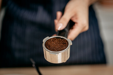 A close-up of a barista’s hand holding a portafilter filled with freshly ground coffee, ready for...