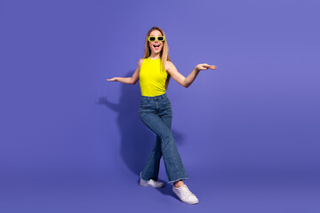 Cheerful young woman in vibrant yellow top and jeans posing confidently against a purple background...