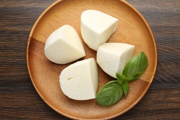 Pieces of delicious mozzarella cheese and basil on wooden table, top view