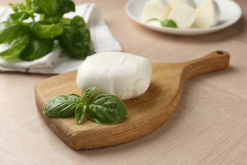 Piece of delicious mozzarella cheese and basil on wooden table, closeup