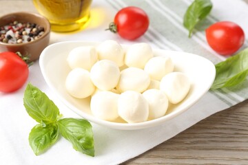 Tasty mozzarella cheese balls, tomatoes, basil, oil and peppercorns on wooden table, closeup