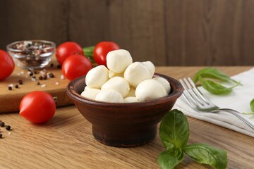 Tasty mozzarella balls, tomatoes, peppercorns and basil on wooden table, closeup