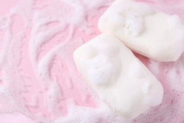 Soap bars with foam on pink background, closeup. Space for text