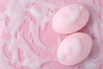 Soap bars with foam on pink background, flat lay. Space for text