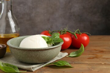 Tasty mozzarella balls, tomatoes, oil and basil on wooden table, closeup