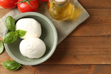 Tasty mozzarella balls, tomatoes, oil and basil on wooden table, flat lay. Space for text