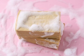 Soap bars with foam on pink background, closeup