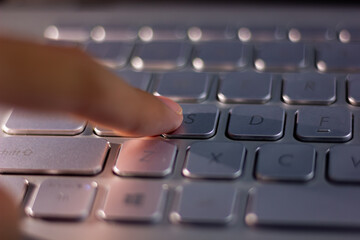 Close-up of a finger pressing a key on a silver metallic laptop keyboard. A concept of work,...