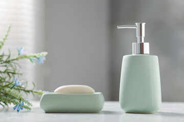 Soap bar, bottle of cosmetic product and flowers on white table indoors, closeup