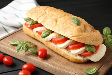 Tasty sandwich with mozzarella cheese, tomatoes and basil on black wooden table, closeup