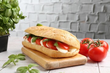 Tasty sandwich with mozzarella cheese, tomatoes and basil on light tiled table against grey textured wall, closeup