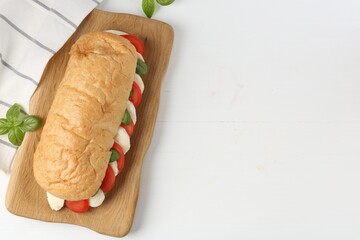 Tasty sandwich with mozzarella cheese, tomatoes and basil on white wooden table, flat lay. Space...