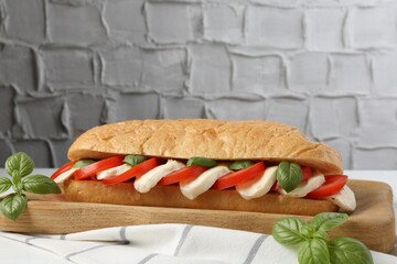 Tasty sandwich with mozzarella cheese, tomatoes and basil on white table against grey textured wall, closeup. Space for text