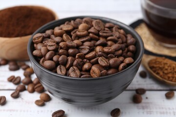 Roasted beans in bowl and different types of instant coffee on white wooden table, closeup