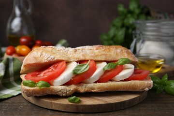 Tasty sandwich with mozzarella cheese, tomatoes and basil on wooden table against brown background, closeup