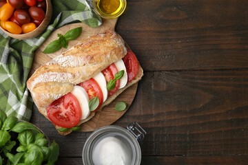 Tasty sandwich with mozzarella cheese, tomatoes and basil on wooden table, flat lay. Space for text