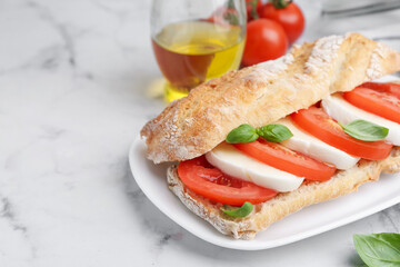 Tasty sandwich with mozzarella cheese, tomatoes and basil on white marble table, closeup. Space for text