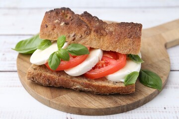 Tasty sandwich with mozzarella cheese, tomatoes and basil on white wooden table, closeup