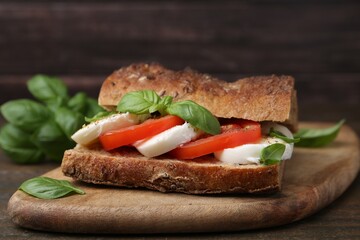 Tasty sandwich with mozzarella cheese, tomatoes and basil on wooden table, closeup