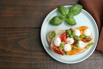 Tasty sandwich with mozzarella cheese, tomatoes and basil on wooden table, top view. Space for text