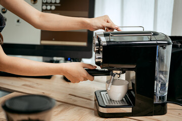 A young Asian female barista in a striped apron carefully pours steamed milk to create intricate latte art, working in a cozy modern café with professional coffee equipment and takeaway cups.