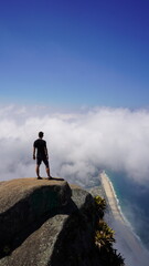 Epic aerial view from Pedra da G&aacute;vea in Rio de Janeiro, showcasing dramatic cliffs, lush rainforest, and the stunning coastline merging with clouds and the Atlantic Ocean