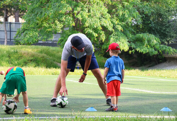  little three-year-old boy plays football at a sports school with a coach.