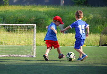  little three-year-old boys plays football at a sports school with a coach.