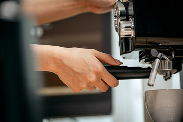 A young Asian female barista in a striped apron carefully pours steamed milk to create intricate latte art, working in a cozy modern café with professional coffee equipment and takeaway cups.