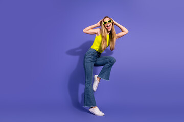 Cheerful young woman in casual outfit posing energetically on a vibrant purple background,...