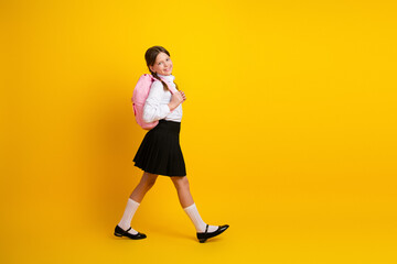 Smiling schoolgirl in uniform with a pink backpack against a vibrant yellow background