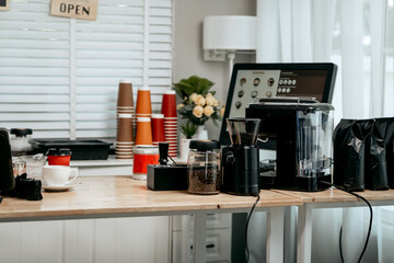 A digital coffee menu is displayed on a computer screen in a modern café, surrounded by stacks of takeaway cups, flowers, a coffee grinder, and brewing equipment