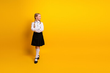 Young schoolgirl in uniform standing confidently against a bright yellow background