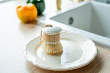 Plate with an ecobrush for washing dishes near the sink, soap in a glass bottle, a towel.