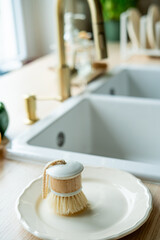 Plate with an ecobrush for washing dishes near the sink, soap in a glass bottle, a towel.