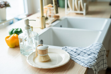 Plate with an ecobrush for washing dishes near the sink, soap in a glass bottle, a towel.