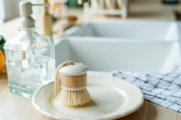 Plate with an ecobrush for washing dishes near the sink, soap in a glass bottle, a towel.