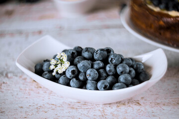 Bowl of vibrant blueberries sits on rustic surface, accentuated by delicate white flowers nearby.