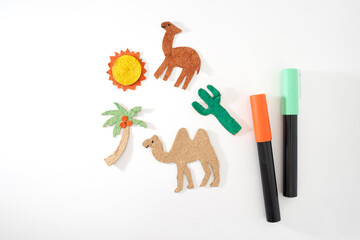 Colored paper cutouts of camel, cactus, palm tree, sun on white background. flat lay of DIY craft elements for desert diorama. Educational and creative project for children. Desert animals