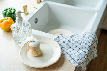 Plate with an ecobrush for washing dishes near the sink, soap in a glass bottle, a towel.