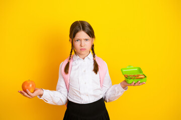 Schoolgirl in uniform holding an apple and lunchbox against a bright yellow backdrop showcasing healthy choices.