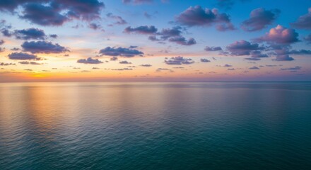 Fototapeta premium Serene sunset over calm ocean; pastel hues paint the sky and reflect on tranquil waters