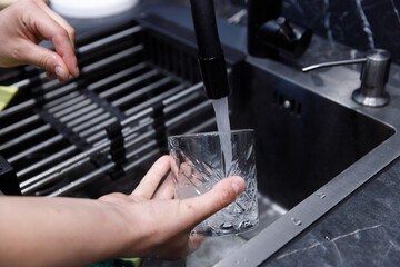 A Person Washing a Textured Glass in a Modern Kitchen Sink Under Running Water Captured in an Elegant and Clean Atmosphere for Optimal Hygiene and Home Maintenance