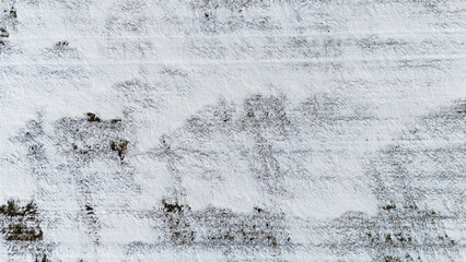 Drone view over a snow covered agriculture field with cultivated rows from crops.