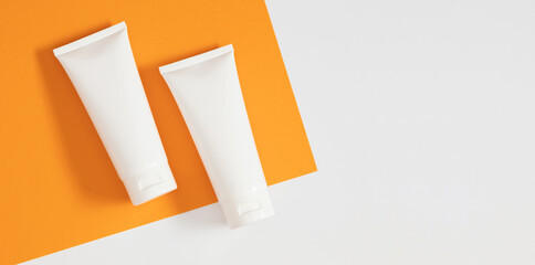 White plastic tube with sunscreen on orange and white background with shadow. Two bottles of sunscreen.