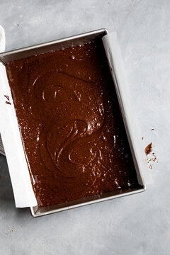 A baking tray filled with chocolate batter lined with parchment paper on a light gray surface.